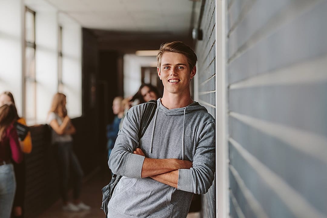 A young male university student standing and leaning to a wall in college corridor.